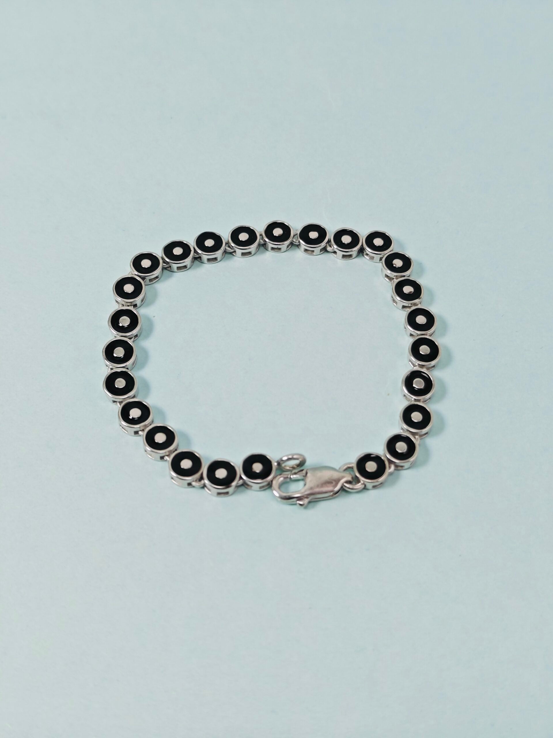 Silver bracelet with black beads on a light blue background